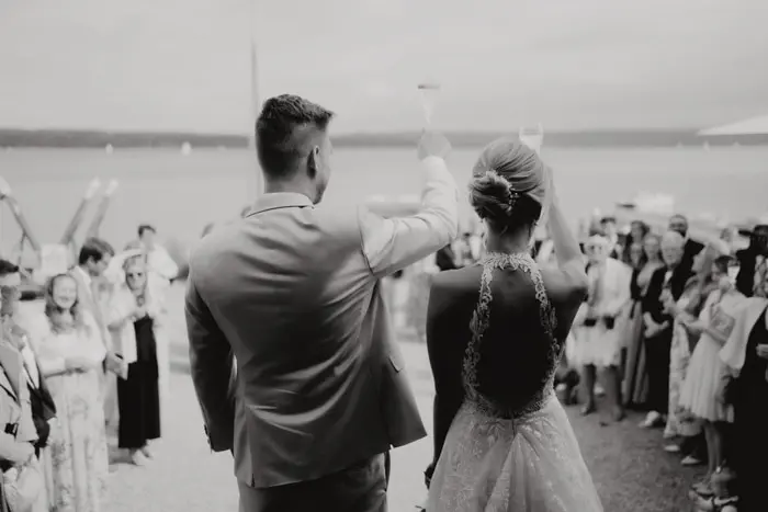 Hochzeitsfotograf Bayern Hochzeitspaar begrüßt Gäste an einem See Dokumentarische Editorial Hochzeitsfotografie