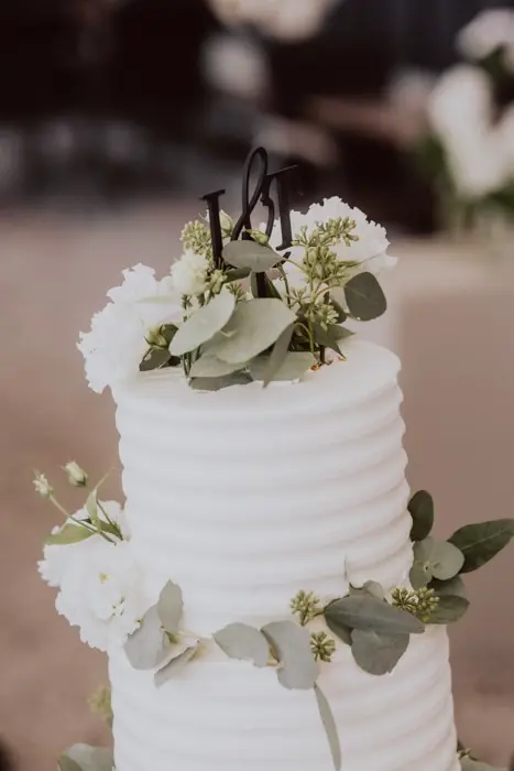 Hochzeitsfotograf Bayern Hochzeitstorte mit grünen Blättern und weißen Blumen dekoriert Dokumentarische Editorial Hochzeitsfotografie
