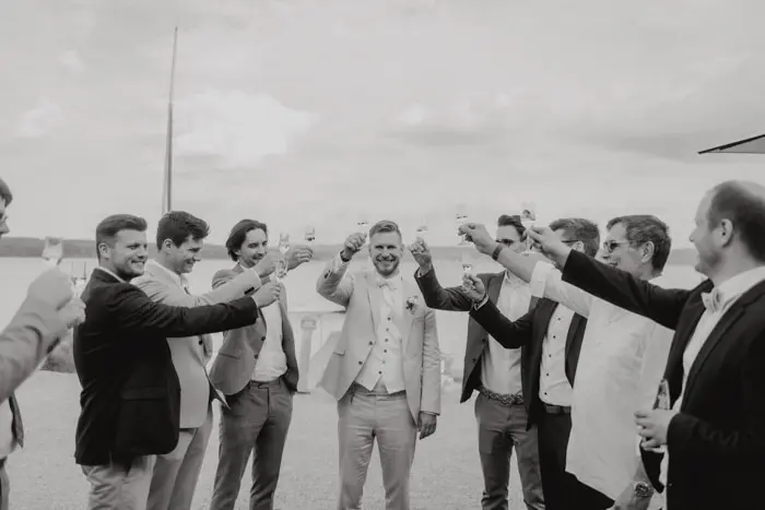 Hochzeitsfotograf Bayern Gruppe von Männern im Anzug stößt freudig im Freien an Dokumentarische Editorial Hochzeitsfotografie