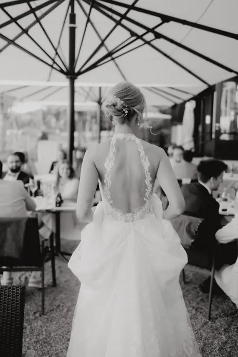 Hochzeitsfotograf Bayern Braut in Hochzeitskleid mit offenem Rücken bei Feier im Freien Dokumentarische Editorial Hochzeitsfotografie