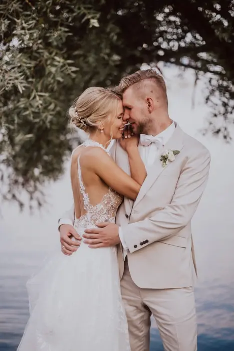 Hochzeitsfotograf Bayern Brautpaar umarmt sich am Seeufer, unter einem Baum Dokumentarische Editorial Hochzeitsfotografie