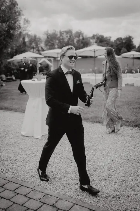Hochzeitsfotograf Bayern Eleganter Mann im Anzug mit Sonnenbrille bei einer Gartengesellschaft Dokumentarische Editorial Hochzeitsfotografie