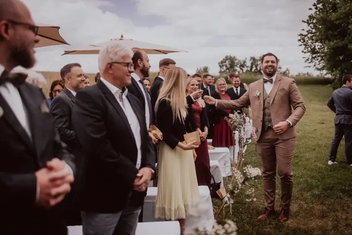 Hochzeitsfotograf Bayern Hochzeitsgäste im Freien, während ein Bräutigam etwas verkündet Dokumentarische Editorial Hochzeitsfotografie