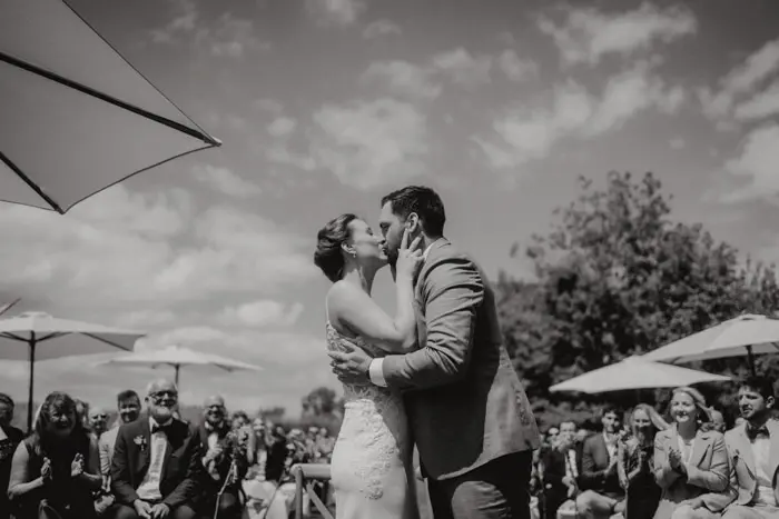 Hochzeitsfotograf Bayern Hochzeitspaar teilt einen Kuss im Freien unter sonnigem Himmel Dokumentarische Editorial Hochzeitsfotografie