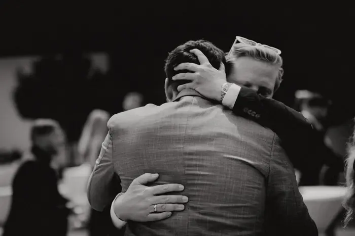 Hochzeitsfotograf Bayern Schwarz-weiß Foto von Umarmung zweier Männer bei Veranstaltung Dokumentarische Editorial Hochzeitsfotografie