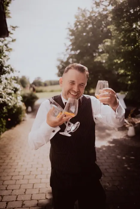 Hochzeitsfotograf Bayern Fröhlicher Mann feiert im Freien mit Weingläsern Dokumentarische Editorial Hochzeitsfotografie