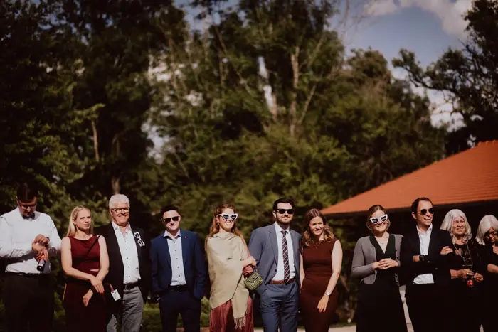 Hochzeitsfotograf Bayern Gruppe von Gästen bei einer Hochzeit im Freien mit Sonnenbrillen Dokumentarische Editorial Hochzeitsfotografie