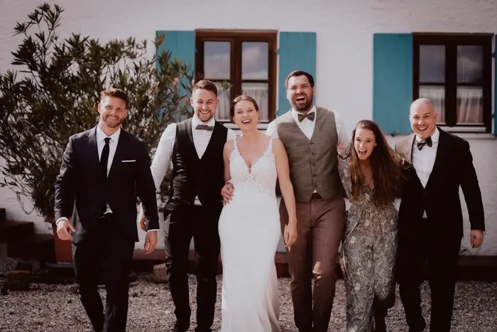 Hochzeitsfotograf Bayern Fröhliche Hochzeitsgesellschaft vor einem Haus mit blauen Fensterläden Dokumentarische Editorial Hochzeitsfotografie