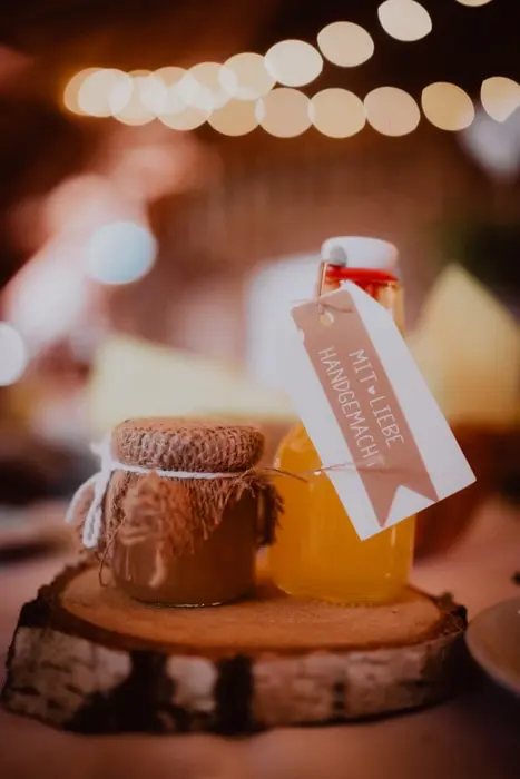 Hochzeitsfotograf Bayern Handgemachte Marmelade und Saft auf rustikalem Holzteller mit Bokeh-Hintergrundlichtern Dokumentarische Editorial Hochzeitsfotografie