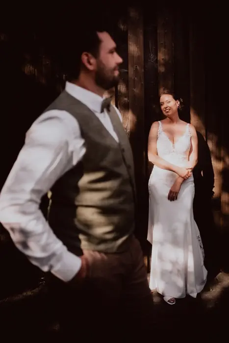 Hochzeitsfotograf Bayern Hochzeitspaar in romantischer Lichtstimmung mit Fokus auf Braut im weißen Kleid Dokumentarische Editorial Hochzeitsfotografie