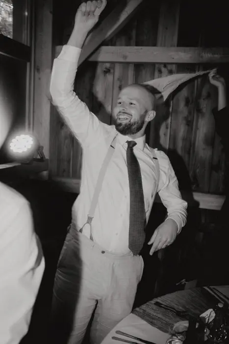 Hochzeitsfotograf Bayern Mann tanzt fröhlich bei einer Feier in einem rustikalen Raum Dokumentarische Editorial Hochzeitsfotografie