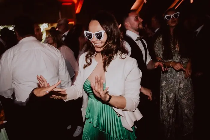 Hochzeitsfotograf Bayern Frau in grüner Kleidung und Herzbrille tanzt auf einer Party Dokumentarische Editorial Hochzeitsfotografie