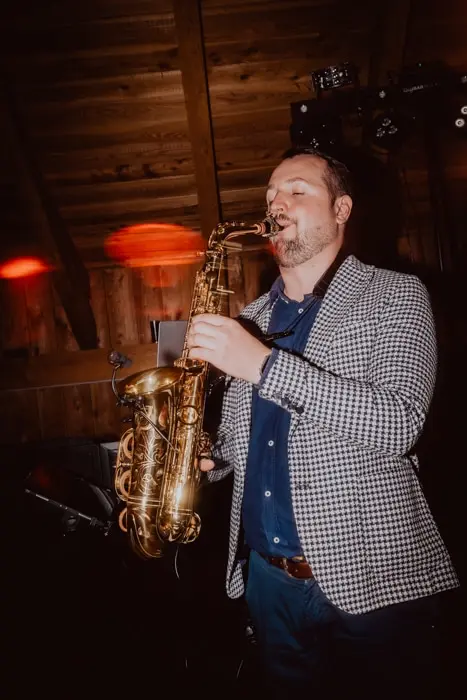 Hochzeitsfotograf Bayern Saxophonist spielt in einem Holzgebäude Dokumentarische Editorial Hochzeitsfotografie