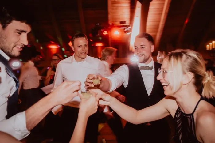 Hochzeitsfotograf Bayern Freunde feiern fröhlich mit Getränken auf einer nächtlichen Party Dokumentarische Editorial Hochzeitsfotografie