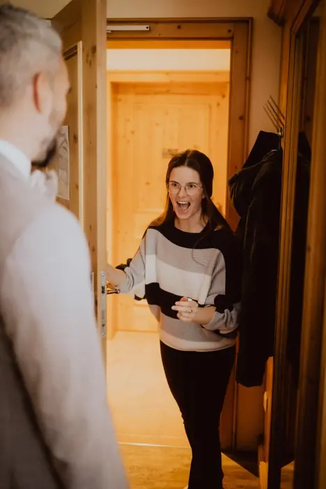 Hochzeitsfotograf Bayern Frau freut sich an einer Tür bei Überraschungsbesuch Dokumentarische Editorial Hochzeitsfotografie