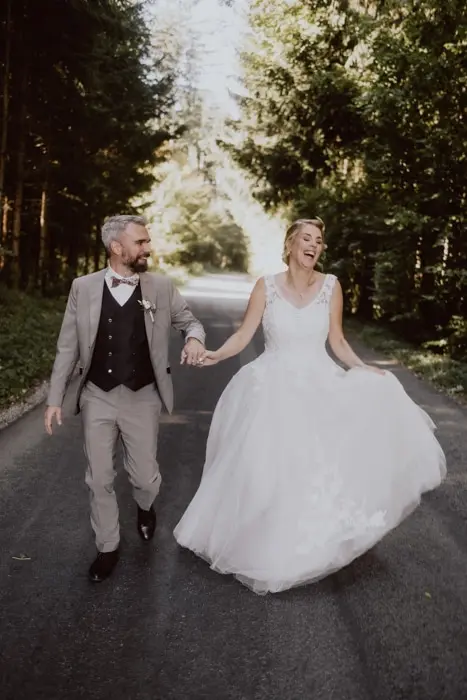 Hochzeitsfotograf Bayern Glückliches Brautpaar spaziert Hand in Hand im Wald Dokumentarische Editorial Hochzeitsfotografie