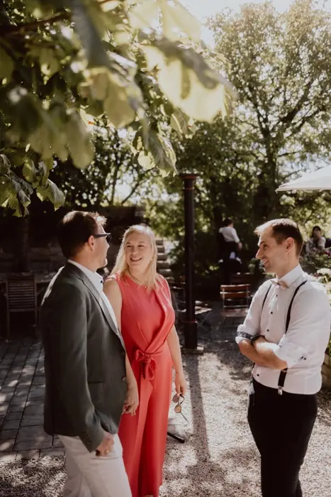 Hochzeitsfotograf Bayern Drei Personen bei einem Gespräch im Freien unter Bäumen Dokumentarische Editorial Hochzeitsfotografie