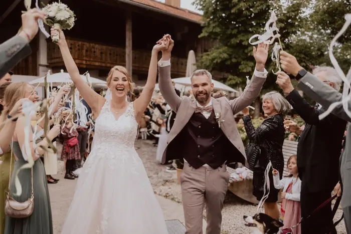 Hochzeitsfotograf Bayern Brautpaar verlässt jubelnd die Hochzeitszeremonie mit Gästen Dokumentarische Editorial Hochzeitsfotografie