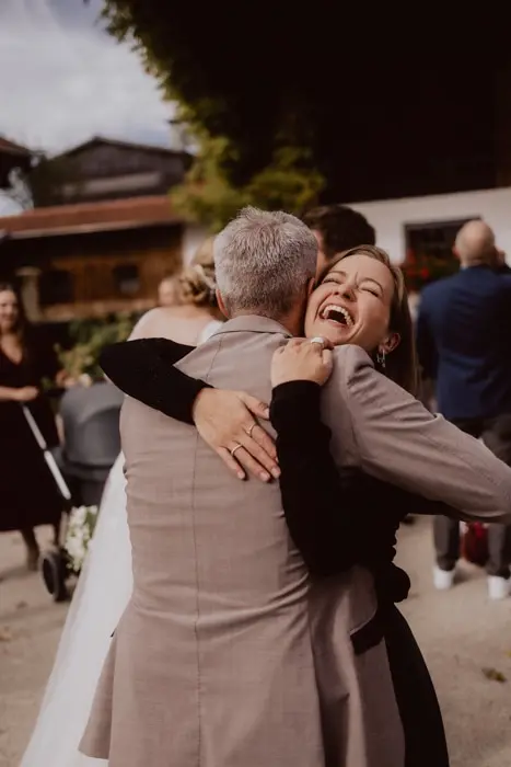 Hochzeitsfotograf Bayern Frau umarmt Mann bei Hochzeitsfeier, beide lächeln Dokumentarische Editorial Hochzeitsfotografie