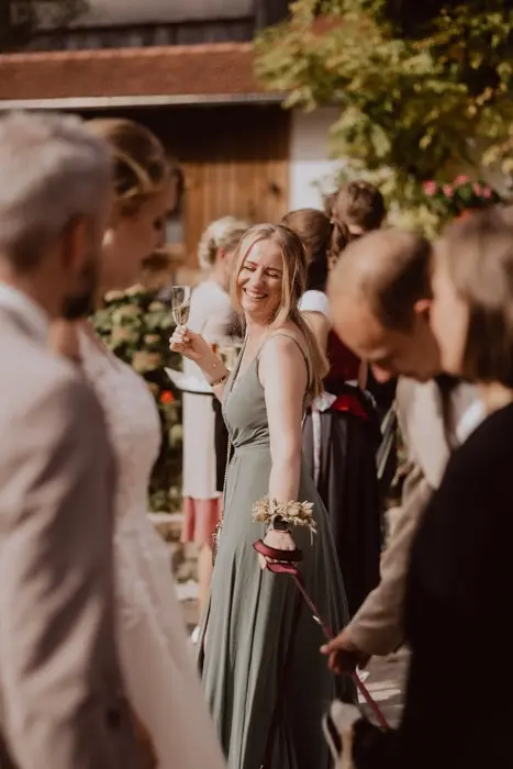 Hochzeitsfotograf Bayern Personen auf einer Hochzeit im Freien, eine Frau lächelnd mit Weinglas Dokumentarische Editorial Hochzeitsfotografie