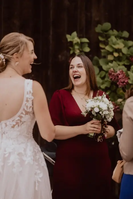 Hochzeitsfotograf Bayern Lachende Frauen bei einer Hochzeit mit Blumenstrauß Dokumentarische Editorial Hochzeitsfotografie