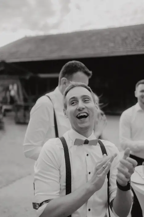 Hochzeitsfotograf Bayern Mann in Anzug mit Fliege lächelnd auf einer Hochzeit im Freien Dokumentarische Editorial Hochzeitsfotografie