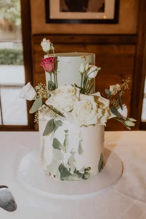 Hochzeitsfotograf Bayern Zweistöckige Hochzeitstorte mit grüner Zuckerglasur und weißen Rosen Dokumentarische Editorial Hochzeitsfotografie