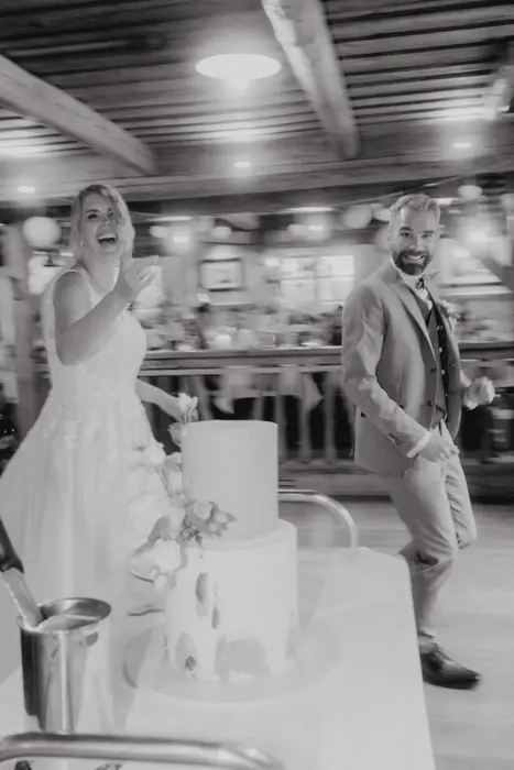 Hochzeitsfotograf Bayern Glückliches Brautpaar tanzt bei der Hochzeit neben einer Hochzeitstorte Dokumentarische Editorial Hochzeitsfotografie