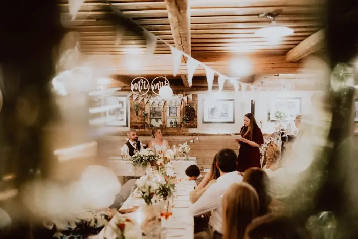 Hochzeitsfotograf Bayern Hochzeitsfeier mit Gästen und Brautpaar in rustikalem Saal Dokumentarische Editorial Hochzeitsfotografie