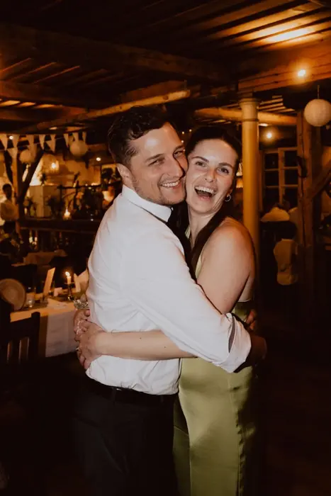 Hochzeitsfotograf Bayern Fröhliches Paar umarmt sich auf Feier in gemütlichem Restaurant Dokumentarische Editorial Hochzeitsfotografie