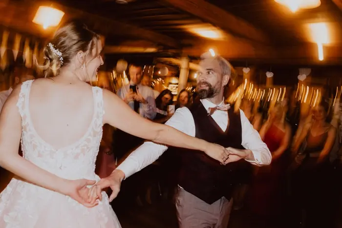 Hochzeitsfotograf Bayern Brautpaar tanzt fröhlich auf Hochzeit mit verschwommenen Gästen Dokumentarische Editorial Hochzeitsfotografie