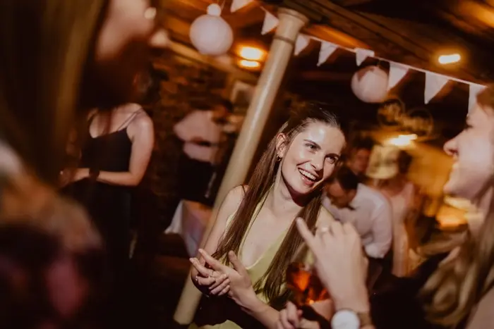 Hochzeitsfotograf Bayern Junge Frau lächelt bei einer Party in einem warm beleuchteten Raum Dokumentarische Editorial Hochzeitsfotografie