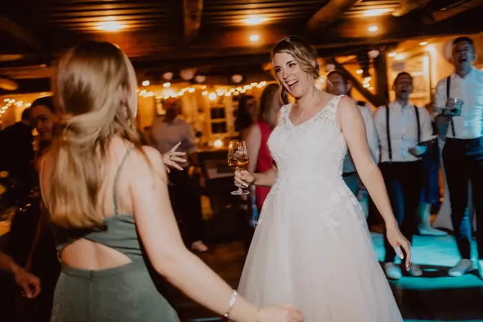 Hochzeitsfotograf Bayern Braut tanzt auf einer Hochzeitsfeier mit Gästen im Hintergrund Dokumentarische Editorial Hochzeitsfotografie