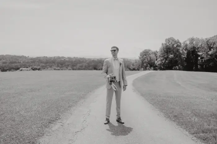 Hochzeitsfotograf Bayern Ein Mann in einem Anzug steht auf einem ländlichen Feldweg Dokumentarische Editorial Hochzeitsfotografie