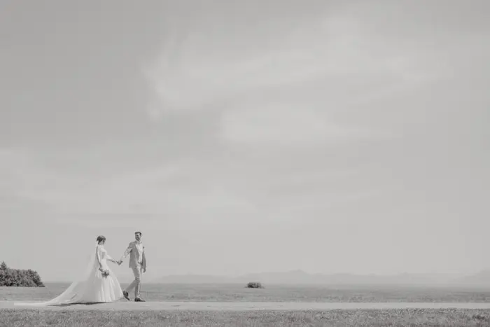 Hochzeitsfotograf Bayern Brautpaar spaziert am Strand entlang vor weitem Himmel Dokumentarische Editorial Hochzeitsfotografie