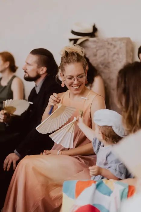 Hochzeitsfotograf Bayern Lachende Frau im Abendkleid spielt mit kleinem Kind bei einer Veranstaltung Dokumentarische Editorial Hochzeitsfotografie