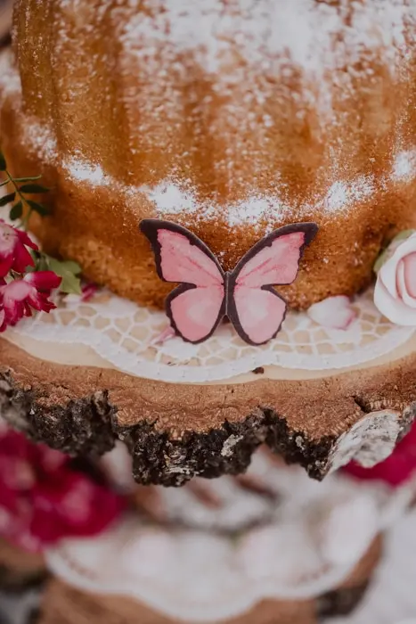 Hochzeitsfotograf Bayern Buttercreme-Torte mit rosa Schmetterling und Blumen verziert Dokumentarische Editorial Hochzeitsfotografie