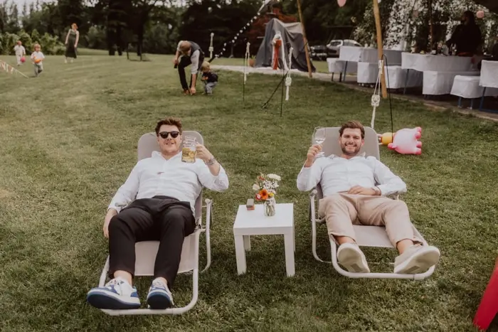 Hochzeitsfotograf Bayern Zwei Männer entspannen mit Getränken im Garten auf Liegestühlen Dokumentarische Editorial Hochzeitsfotografie
