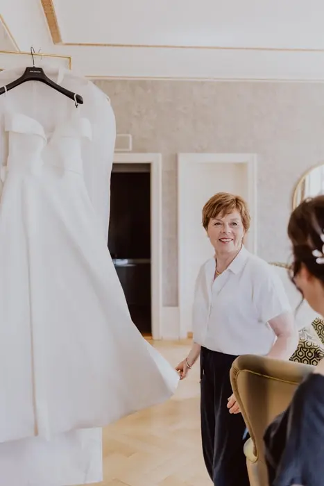 Hochzeitsfotograf Bayern Braut mit Freundin bewundert Hochzeitskleid im eleganten Raum Dokumentarische Editorial Hochzeitsfotografie