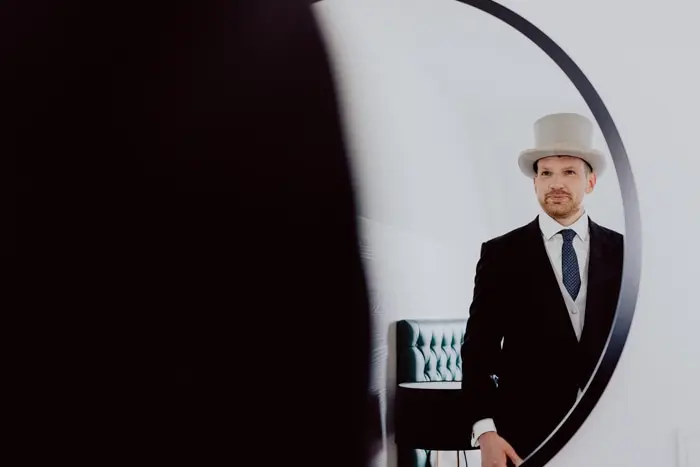 Hochzeitsfotograf Bayern Mann im Anzug mit Zylinder vor rundem Spiegel Dokumentarische Editorial Hochzeitsfotografie