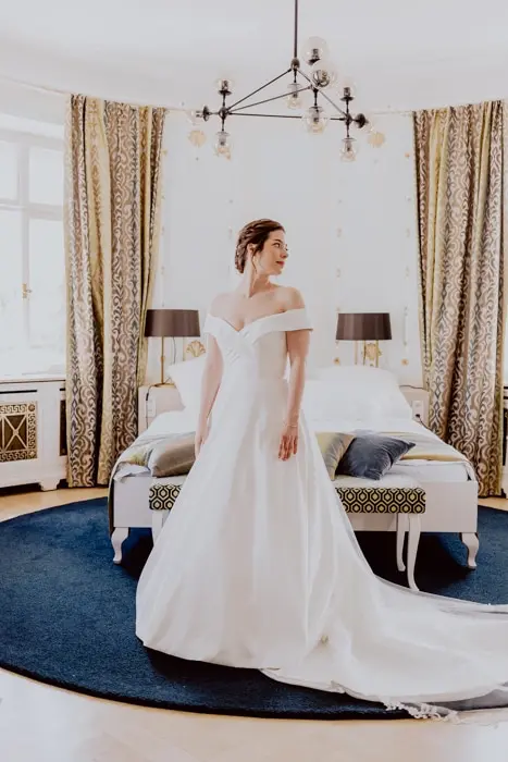 Hochzeitsfotograf Bayern Hochzeitskleid-Braut steht im eleganten Schlafzimmer Dokumentarische Editorial Hochzeitsfotografie