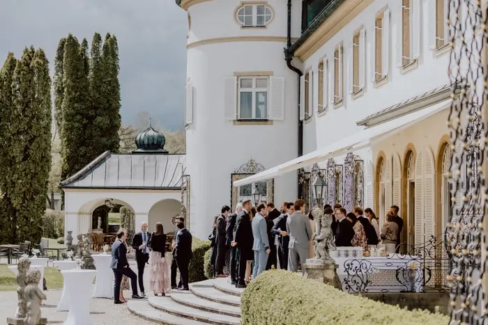 Hochzeitsfotograf Bayern Gäste versammeln sich bei einer Hochzeitsfeier in einem eleganten Schlossgarten Dokumentarische Editorial Hochzeitsfotografie