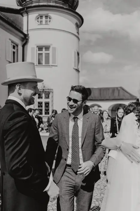 Hochzeitsfotograf Bayern Schwarz-Weiß-Foto einer fröhlichen Hochzeitsgesellschaft vor einem historischen Gebäude Dokumentarische Editorial Hochzeitsfotografie