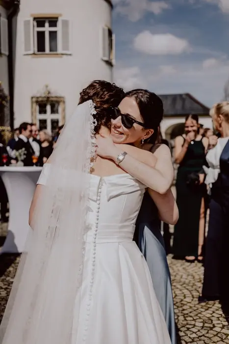 Hochzeitsfotograf Bayern Braut und Freundin umarmen sich auf einer Hochzeitsfeier im Freien Dokumentarische Editorial Hochzeitsfotografie