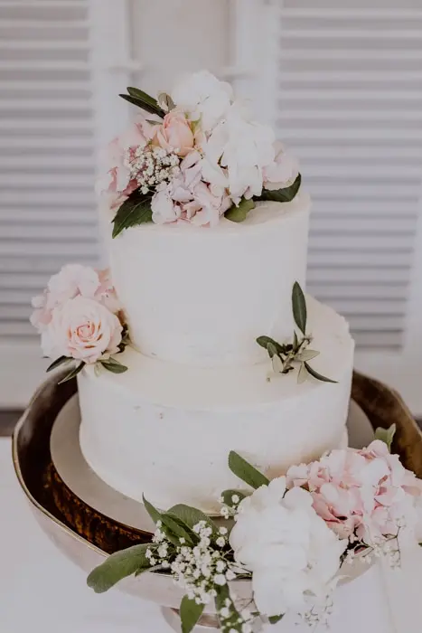Hochzeitsfotograf Bayern Zweistöckige Hochzeitstorte mit rosa und weißen Blumen Dokumentarische Editorial Hochzeitsfotografie