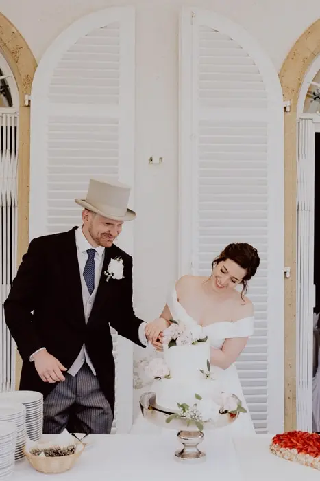 Hochzeitsfotograf Bayern Brautpaar schneidet Hochzeitstorte bei Feier in elegantem Ambiente Dokumentarische Editorial Hochzeitsfotografie