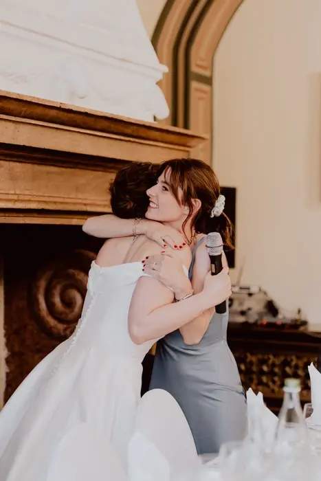 Hochzeitsfotograf Bayern Zwei Frauen umarmen sich bei einer Hochzeit, eine hält ein Mikrofon Dokumentarische Editorial Hochzeitsfotografie