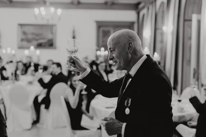 Hochzeitsfotograf Bayern Elegantes Abendessen mit einem Mann, der ein Glas bei einer Feier erhebt Dokumentarische Editorial Hochzeitsfotografie