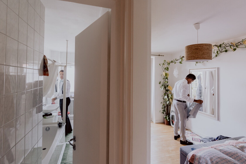 Bräutigam steht beim getting ready vor einem Spiegel in der Wohnung