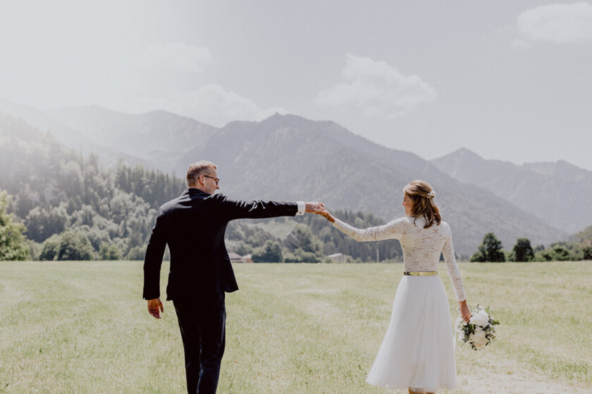 Brautpaar hält Hände vor Bergkulisse auf der auf der Hochzeit auf Gut Kaltenbrunn Tegernsee